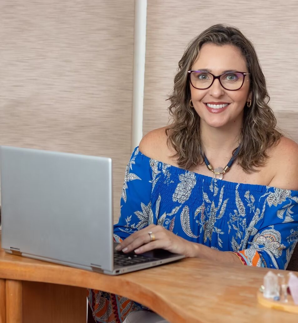 Isabela Gallo sorrindo em seu espaço de atendimento, diante de um notebook